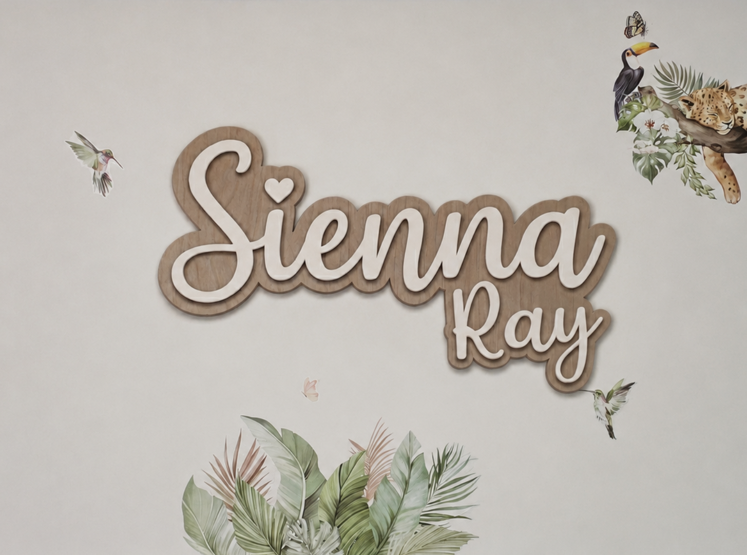 Decorative wall art with 'Sienna Ray' text and nature-themed elements on a light background